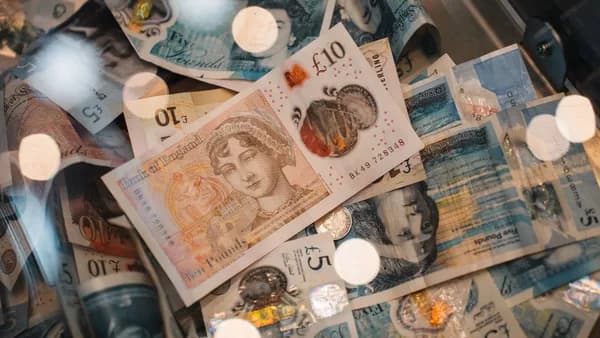 A detailed view of British £5 and £10 pound sterling notes with coins, featuring warm bokeh effects.