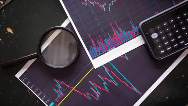 Stock market charts analyzed with a magnifying glass and calculator for financial research.