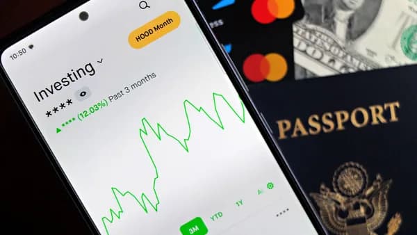Smartphone showing stock market app with travel essentials: passport, money, and cards.