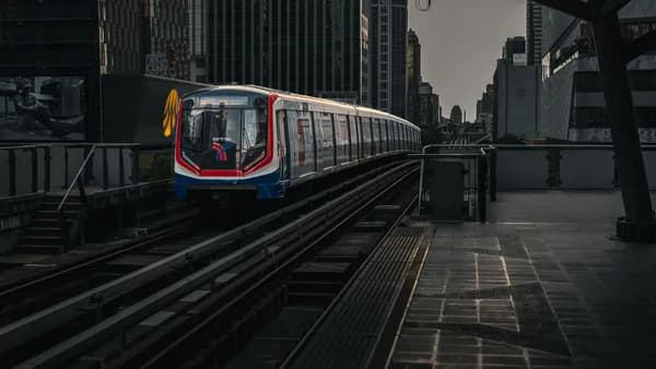A modern train travels on an elevated track amid city skyscrapers at twilight.