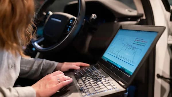 Female engineer using laptop to analyze vehicle data inside a car for testing purposes.