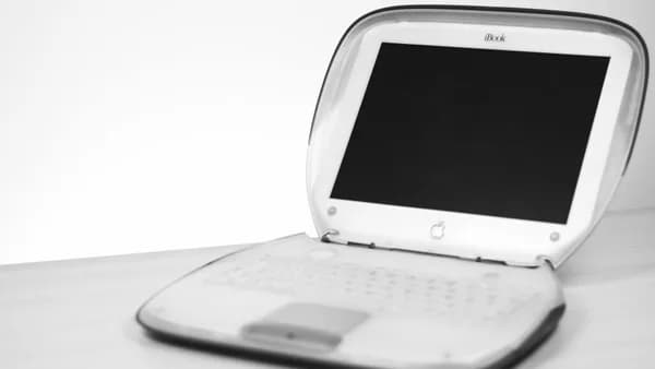 Classic iBook laptop with keyboard and screen displayed on a desk in monochrome.