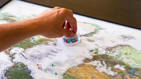 A hand placing colorful pins on a world map, symbolizing travel planning and global exploration.