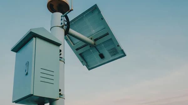 A solar panel paired with a security camera against a clear sky, representing renewable technology.