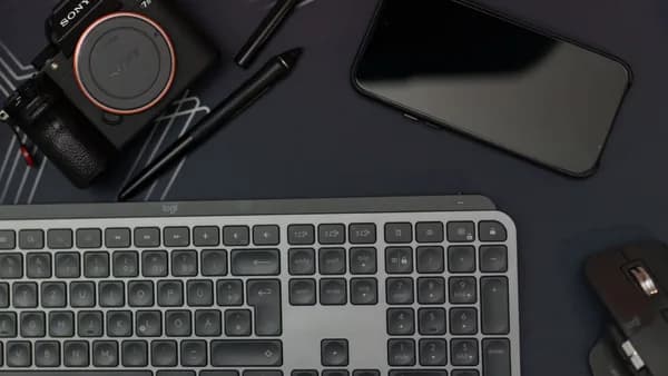 Flat lay of a modern workspace featuring a camera, smartphone, keyboard, and mouse.