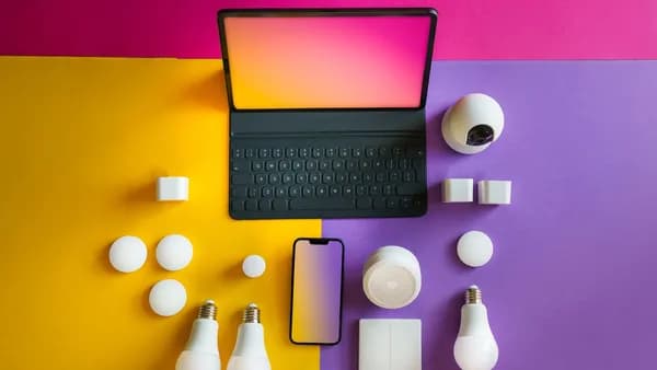 Flat lay of smart home devices including a tablet, smartphone, and bulbs on a vibrant background.