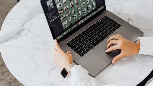 Hands editing photos on laptop, modern workspace on marble table.