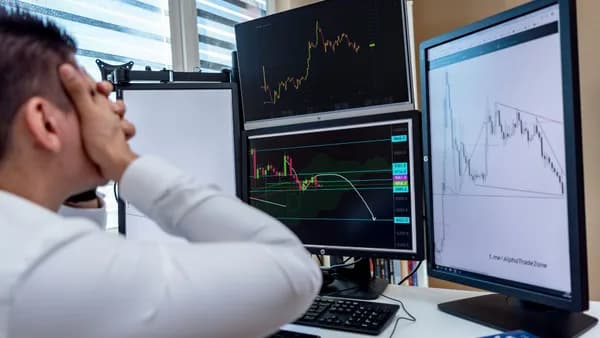 Frustrated man monitoring multiple trading graphs on computer screens in an office setting.