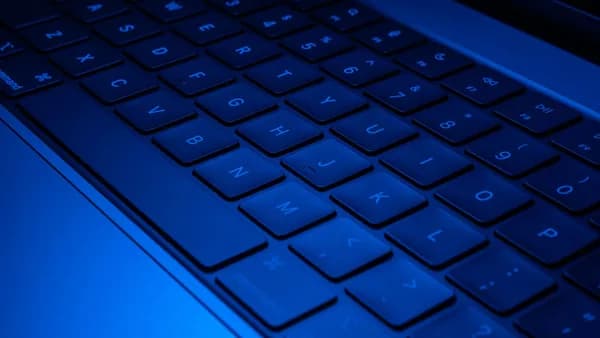 Close-up image of a laptop keyboard illuminated with blue light, showcasing modern technology design.