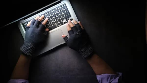 Hacker in fingerless gloves typing on laptop keyboard from above in a dark setting.