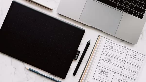 Top-down view of a desk setup including a laptop, drawing tablet, and design sketches.