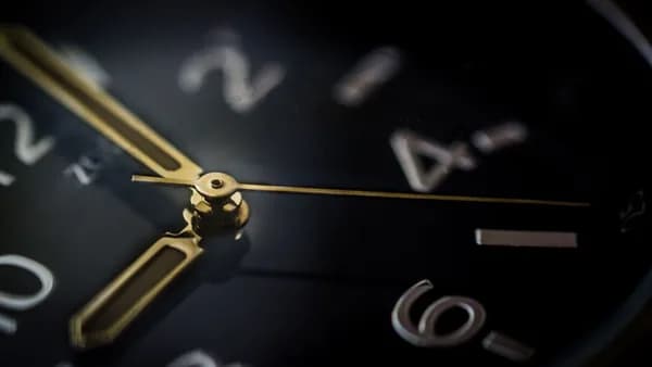Detailed macro shot of an analog wristwatch showing gold hands and blurred numerals.