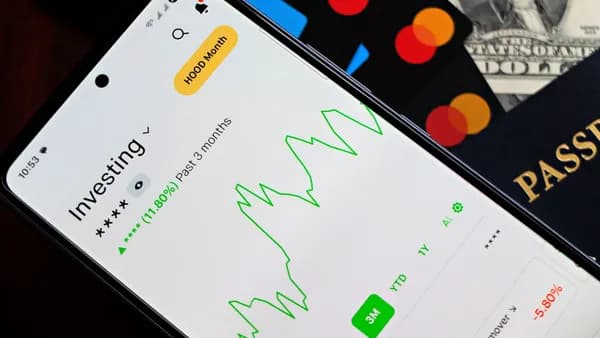 A smartphone showing an investment app with green growth indicators, surrounded by credit cards, US dollars, and a passport.