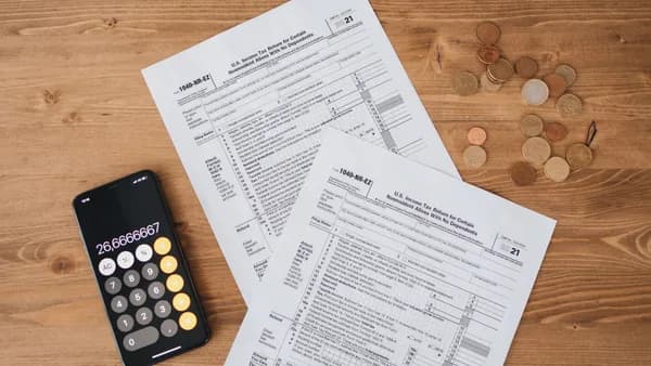 Top view of tax documents, calculator, and coins on wooden table.
