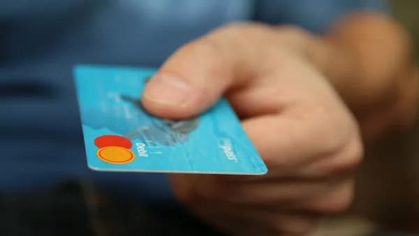 A close-up shot of a hand offering a blue debit card for payment.