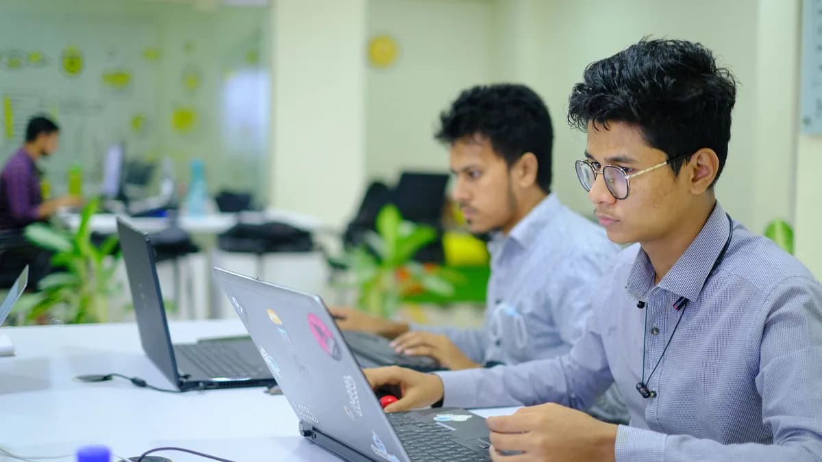 Two young professionals working on laptops in a vibrant and modern office setting.