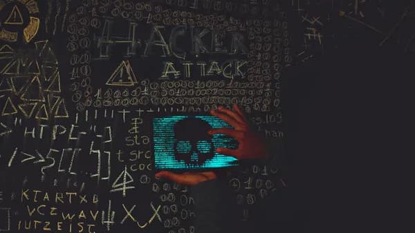 A hacker in a black hoodie using a tablet displaying a skull, surrounded by chalk symbols and 'Hacker Attack' text.
