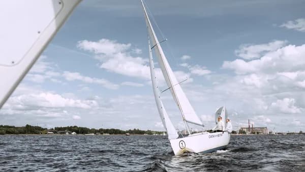 Two people navigating a sailboat on open waters under a bright sky. Ideal for adventure and travel themes.