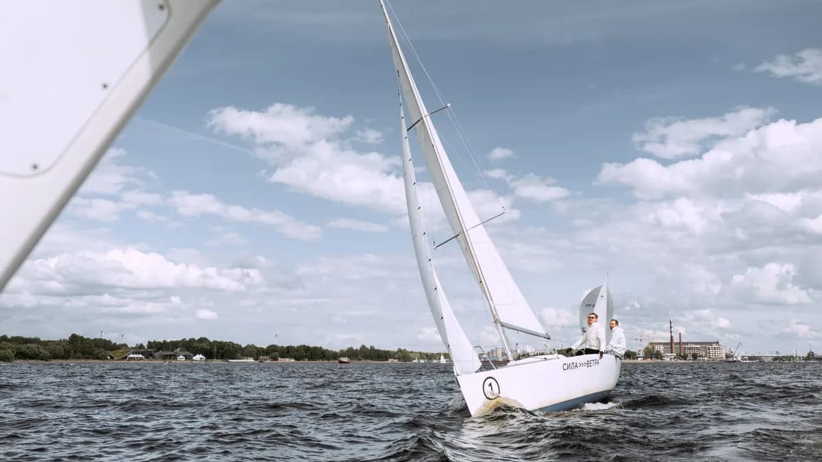 Two people navigating a sailboat on open waters under a bright sky. Ideal for adventure and travel themes.