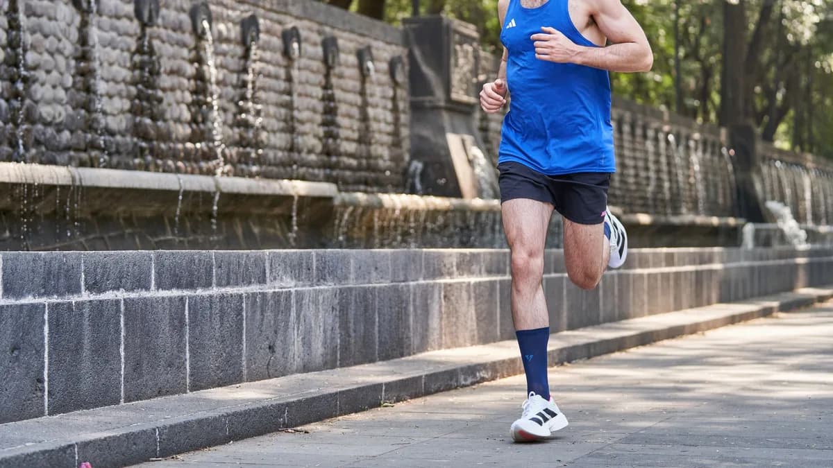 An athletic man jogging near a fountain in an urban park during the day.