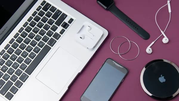 Flat lay of various electronic gadgets on a purple surface including a laptop, smartphone, and smartwatch.