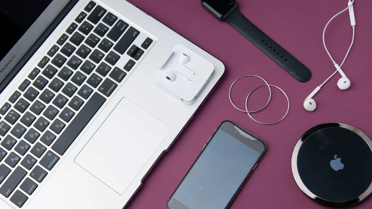 Flat lay of various electronic gadgets on a purple surface including a laptop, smartphone, and smartwatch.