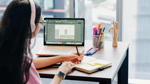 Woman using laptop and notebook in modern home office setup, enhancing productivity.