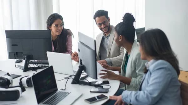 A diverse team engages in discussion around computers in a modern office setting.