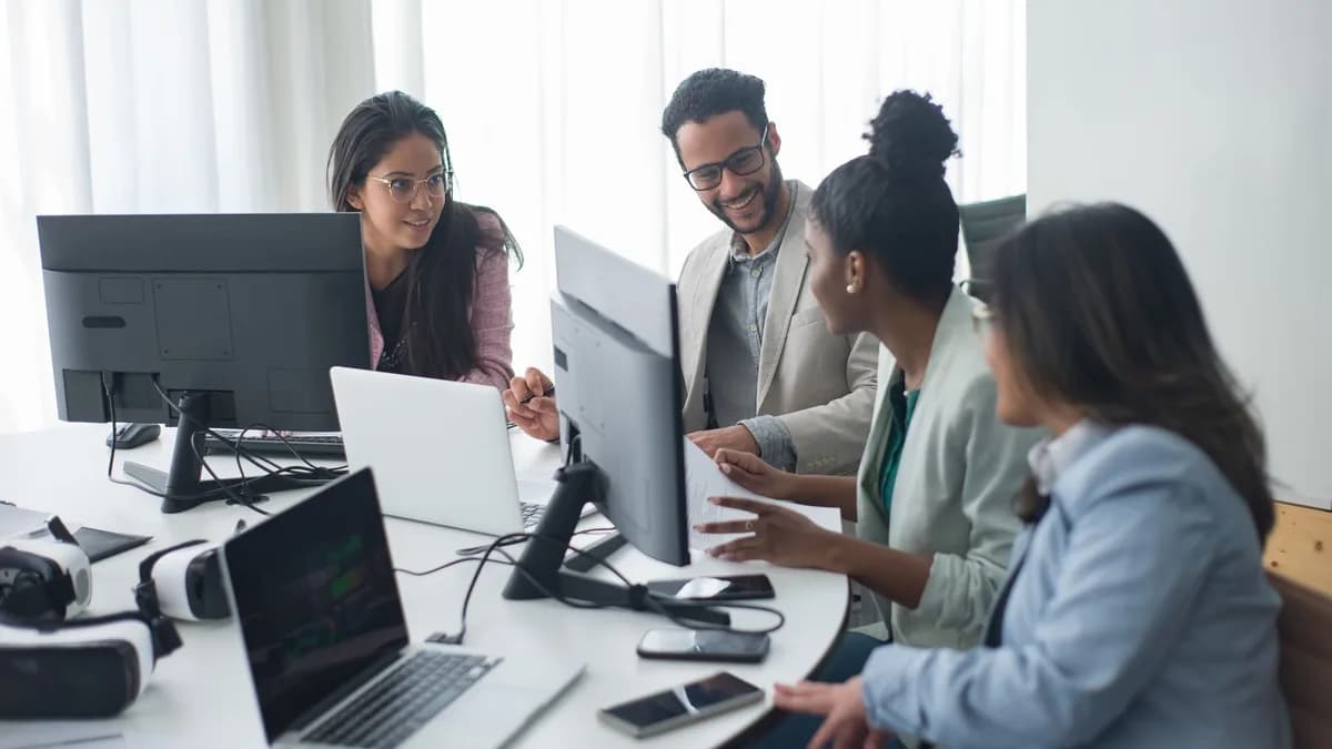 A diverse team engages in discussion around computers in a modern office setting.