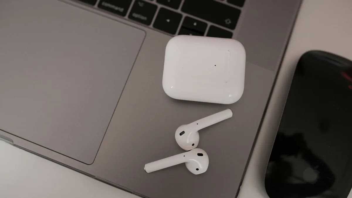 Close-up of wireless earbuds and case on a laptop, highlighting modern tech usage.