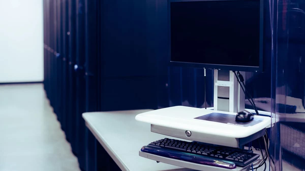 Contemporary computer with black screen placed on stand near row of server steel racks in data center