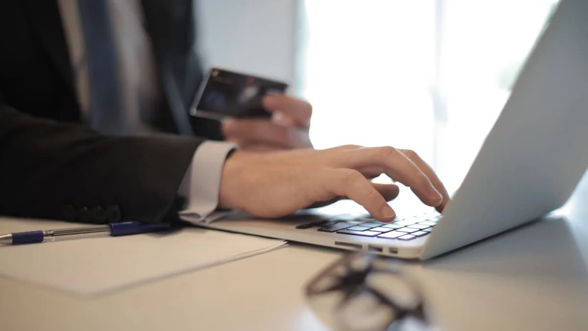 Man in suit using laptop and credit card for online transaction at work.