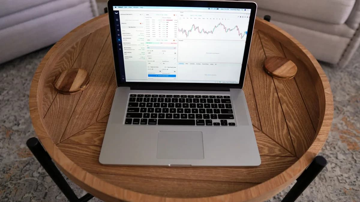 Close-up of a laptop displaying trading charts on a stylish wooden table, ideal for financial themes.
