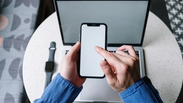 Hands operating a smartphone above a laptop with a smartwatch nearby, showcasing modern technology.