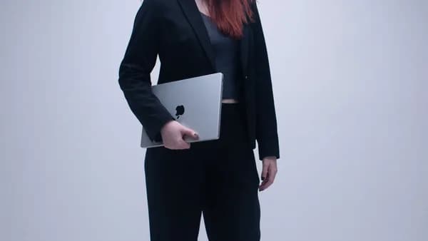 Businesswoman in black suit holding a laptop in an office setting.