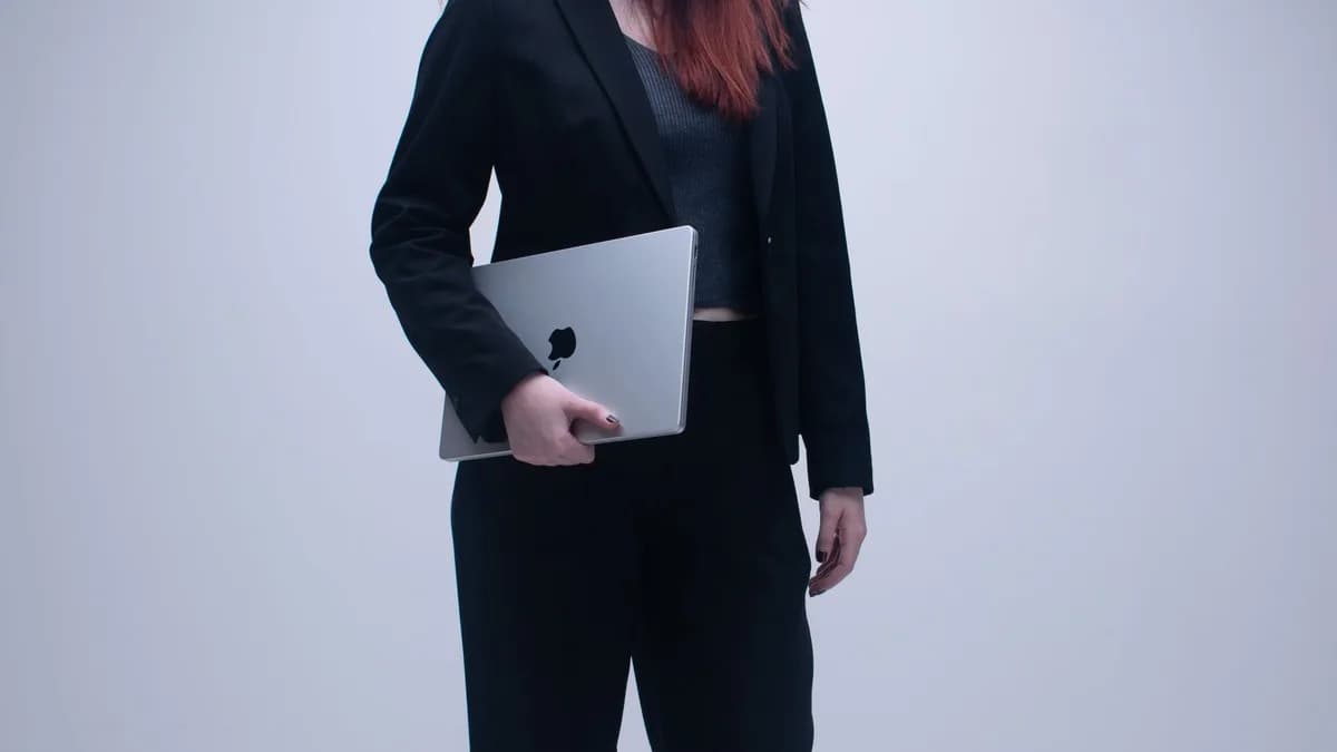 Businesswoman in black suit holding a laptop in an office setting.