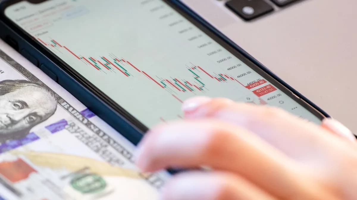 Close-up of a smartphone displaying stock market data over a dollar bill on a desk.