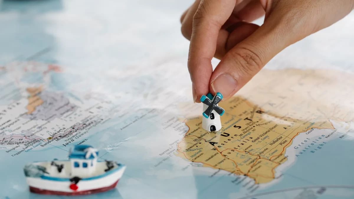 Close-up of a hand placing a tiny windmill on a map, highlighting Australia.