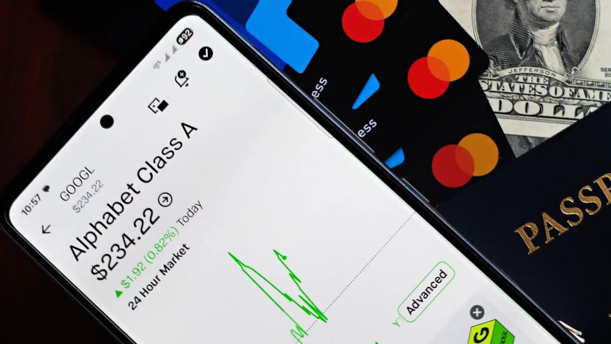 A smartphone displaying Alphabet stock price alongside credit cards, cash, and passport.