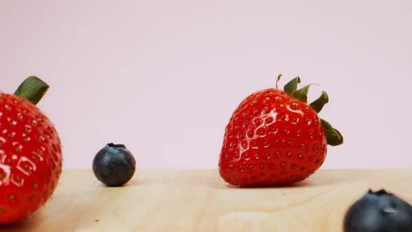 Vivid close-up of strawberries and blueberries on a wooden surface with pink background.