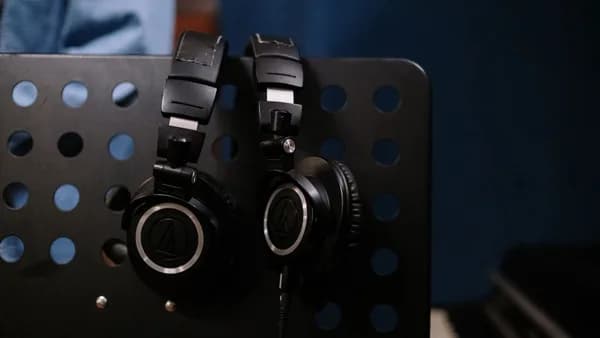Close-up of professional headphones hanging on a perforated music stand in a studio setting.