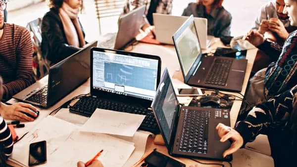 Group of diverse adults collaborating with laptops and papers in a modern office environment.