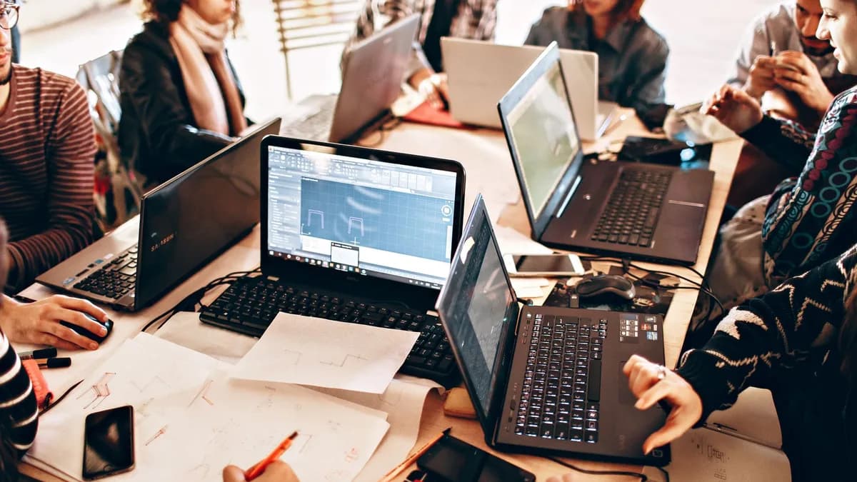 Group of diverse adults collaborating with laptops and papers in a modern office environment.