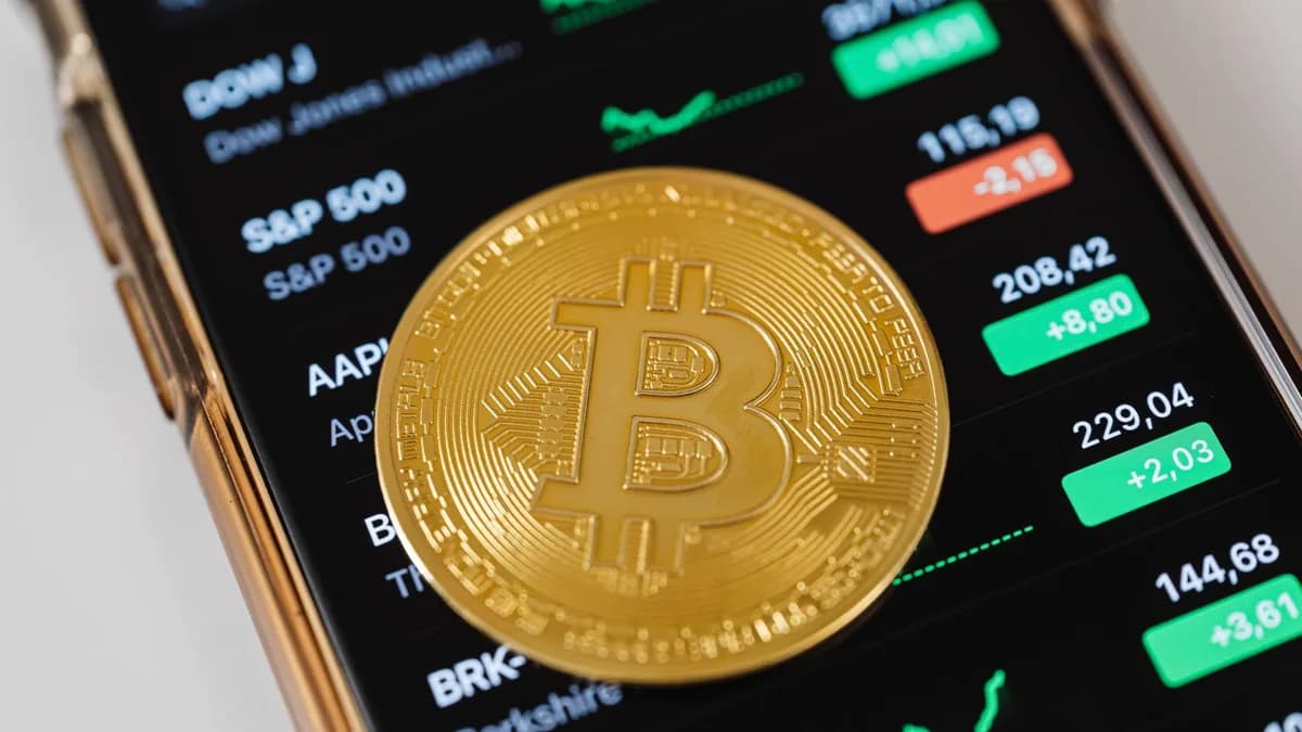 A close-up of a Bitcoin coin placed on a mobile device displaying stock market trading data.