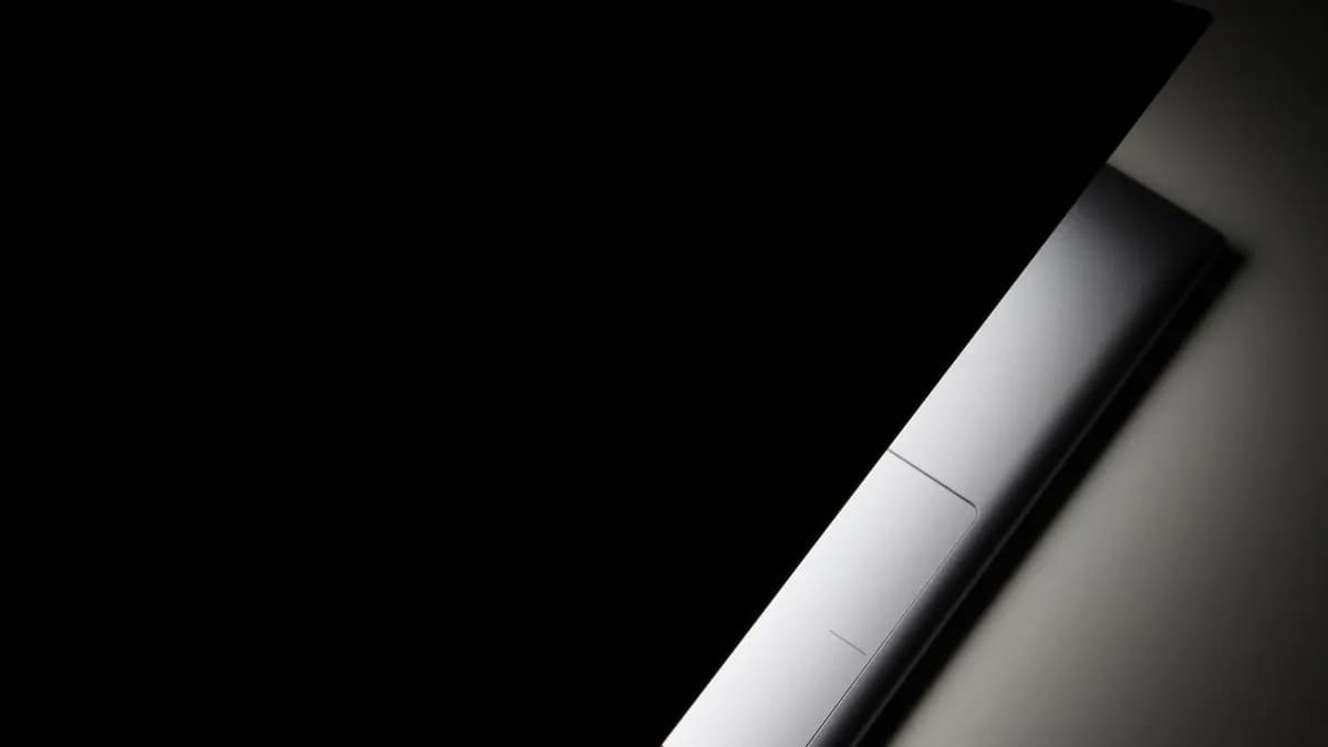A partial view of a modern laptop closed in shadow, highlighting its sleek design.