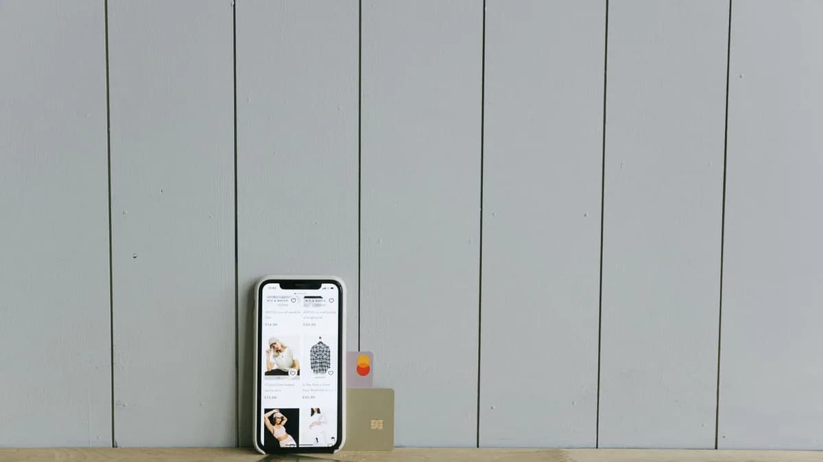 A smartphone displaying an ecommerce site with a credit card, set on a wooden surface, depicting online shopping.