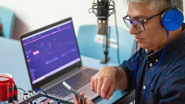 A man using audio equipment and a laptop while recording a podcast with headphones and microphone.