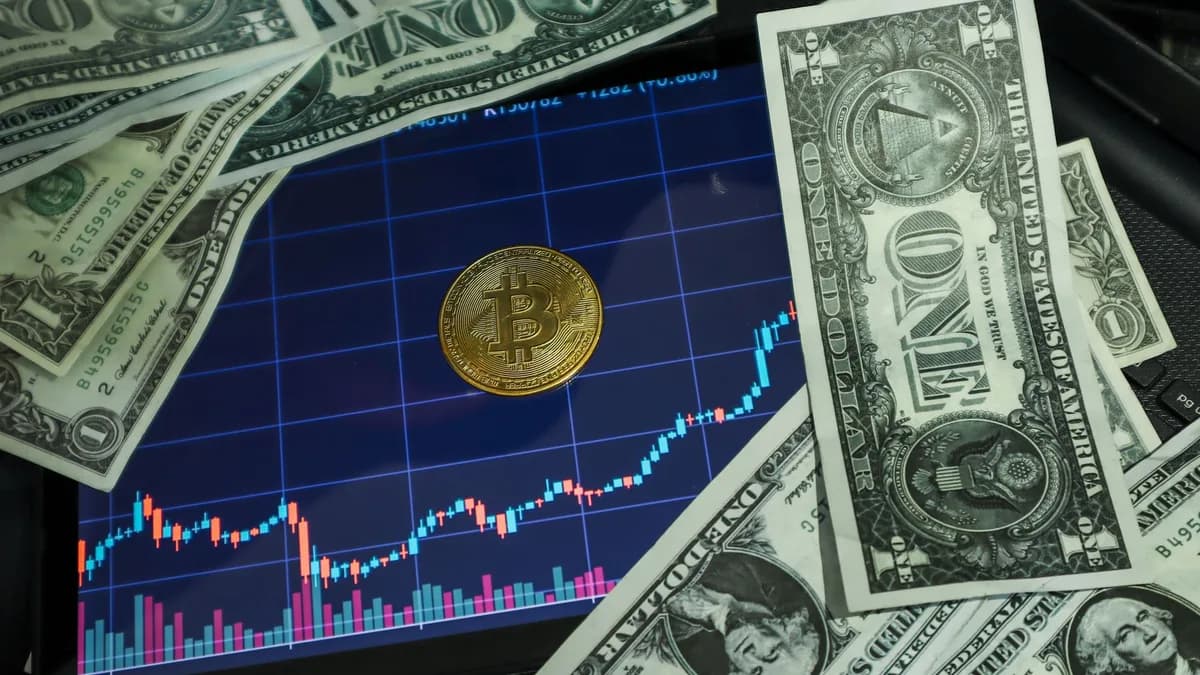 Bitcoin coin on a tablet showing stock chart, surrounded by dollar bills.