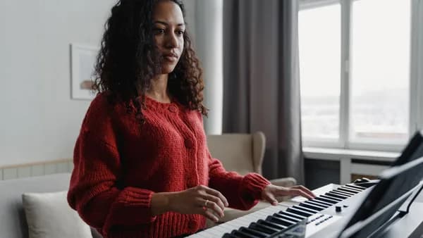 Woman in red sweater focused on playing the piano in a cozy home setting.