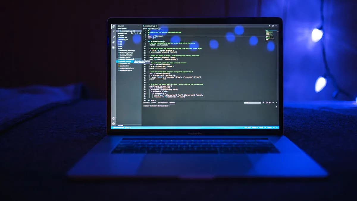 Close-up of a laptop screen displaying code, set against a dark backdrop with blue lighting for a tech-focused ambiance.